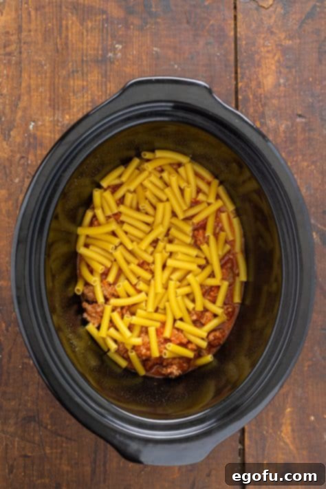 Uncooked ziti noodles layered over the meat sauce in the slow cooker, ready for the next layer of cheese.