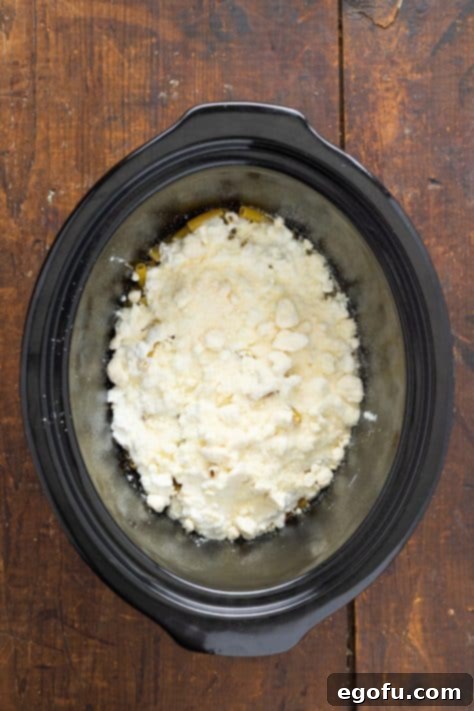 The vibrant layers of meat sauce, pasta, and creamy cottage cheese visibly built up in the slow cooker, ready for the next stage of assembly.