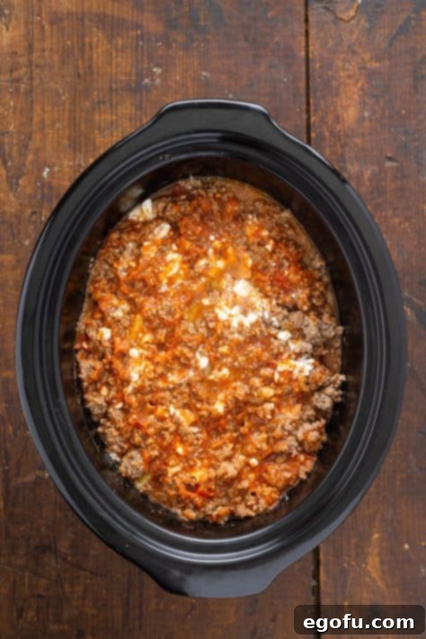 A top-down view of the slow cooker, showcasing all layers of sauce, cheeses, and pasta perfectly arranged and ready for cooking.