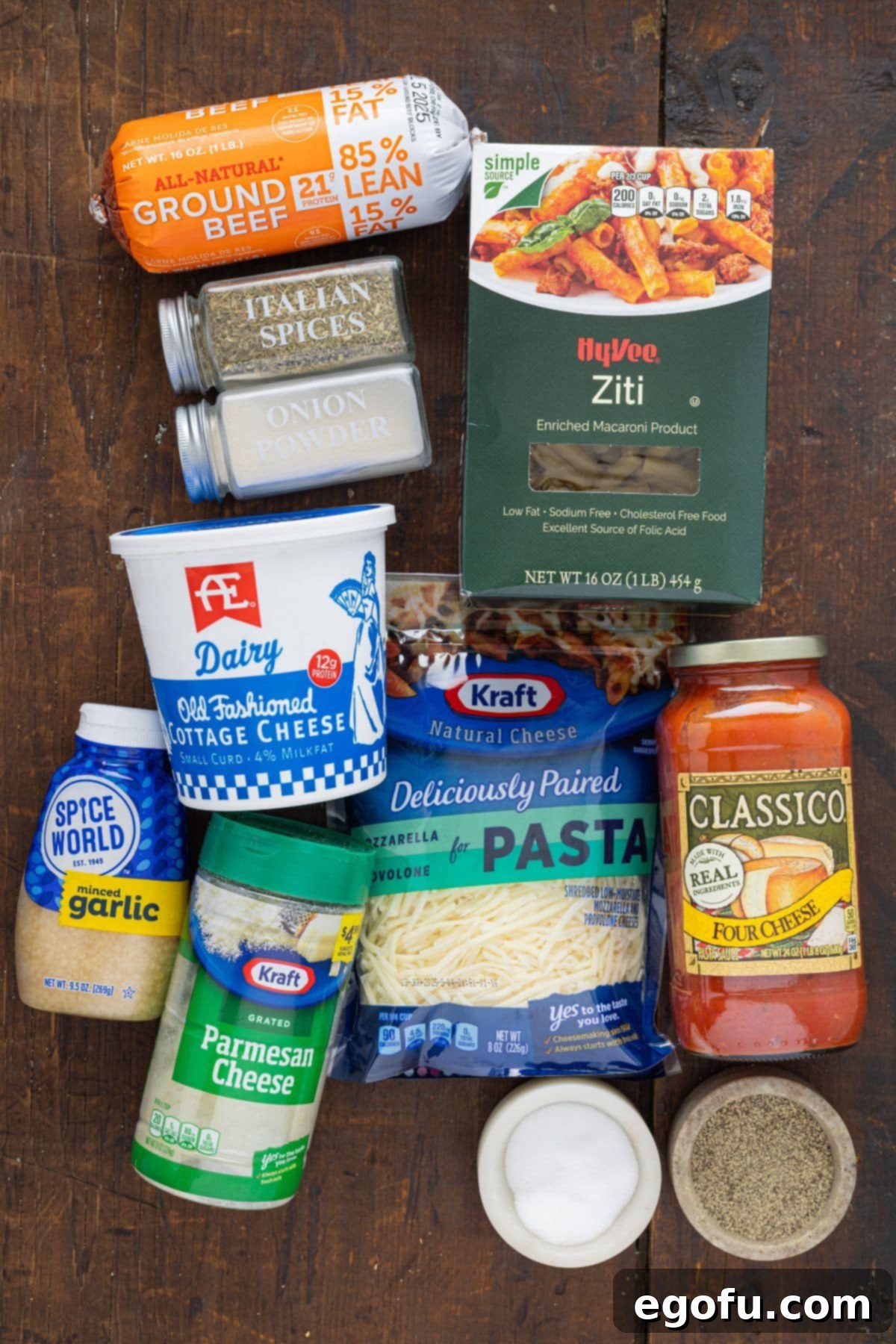 A vibrant flat lay image showcasing all the fresh ingredients needed for Crock Pot Baked Ziti, including ground beef, minced garlic, onion powder, Italian seasoning, marinara sauce, cottage cheese, grated Parmesan cheese, ziti pasta, shredded mozzarella and provolone cheese, and water.