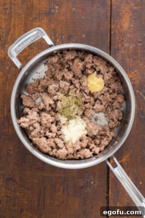 Ground beef cooking in a skillet with aromatic minced garlic, onion powder, and Italian seasoning.
