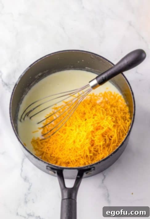 Shredded cheese being added to milk and butter in a pot.