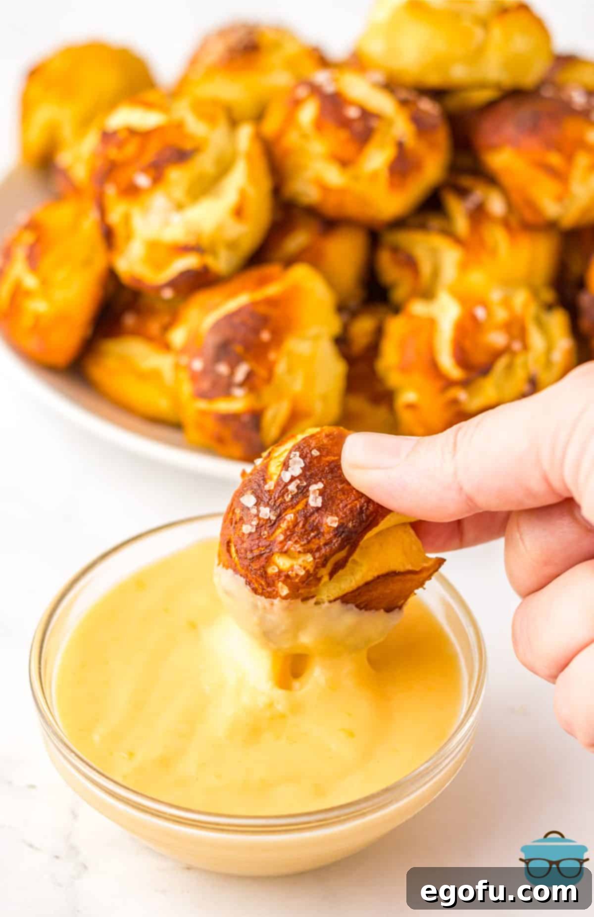 A hand dipping a Biscuit Pretzel Bite into the homemade cheese sauce.