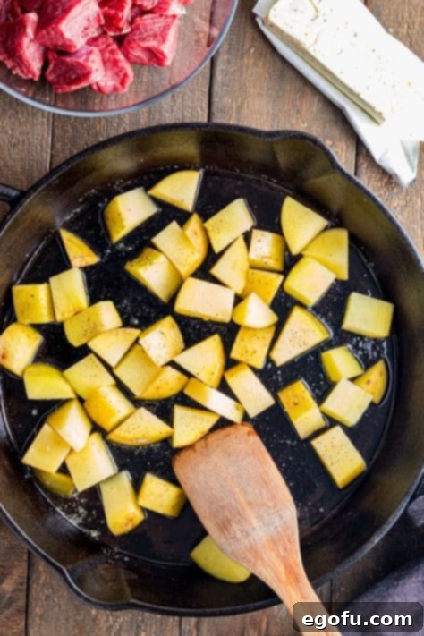 Pan-Seared Garlic Butter Steak Bites with Crispy Potatoes 7 Seasoned potatoes cooking in one section of the skillet, while seasoned steak bites are added to the other side for searing.