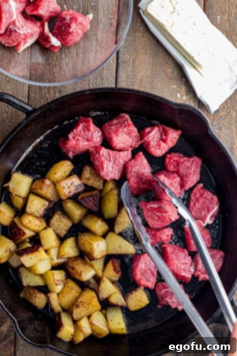 Pan-Seared Garlic Butter Steak Bites with Crispy Potatoes 9 A fork holding a single Garlic Butter Steak Bite, poised above a plate of the finished dish.