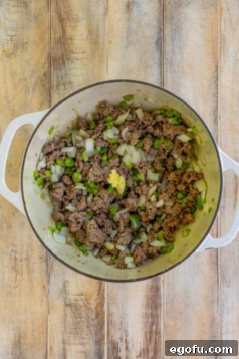 A deep skillet with onions, peppers, garlic, and ground beef.