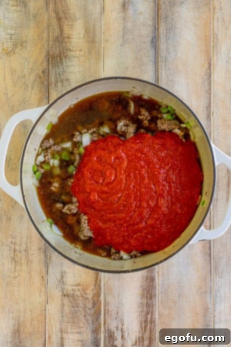 Beef broth and marinara being added to a deep skillet with other ingredients.