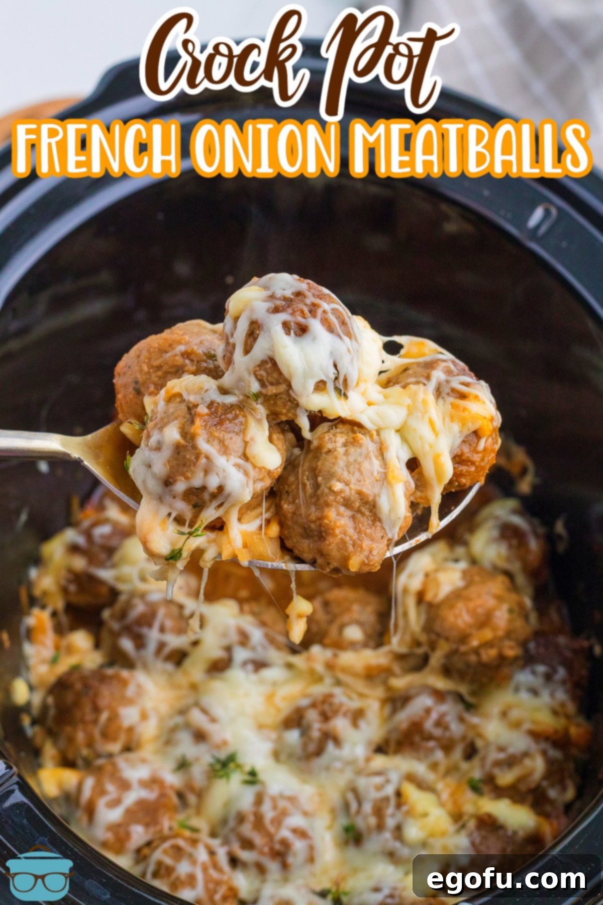 A serving spoon lifting a portion of Crock Pot French Onion Meatballs from the slow cooker, showcasing the rich broth and melted cheese.