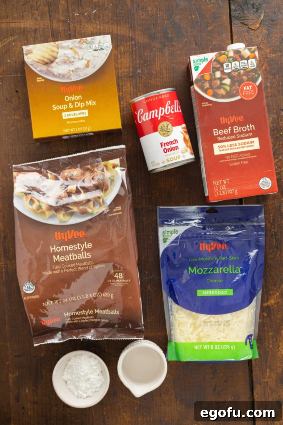 Collection of main ingredients: frozen meatballs, a can of French Onion Soup, a packet of French Onion Soup Mix, beef broth, shredded mozzarella cheese, and cornstarch, ready for assembly.