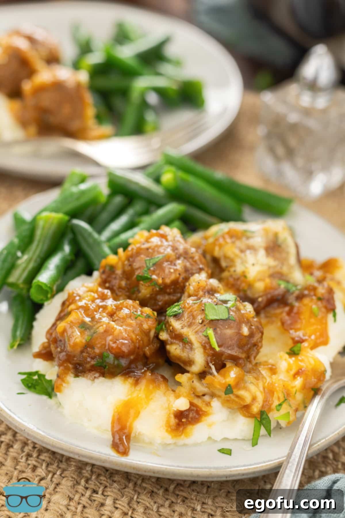 French Onion Meatballs served over a bed of creamy mashed potatoes, accompanied by a vibrant side of green beans, ready to be enjoyed.
