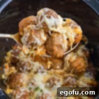 A scoop of Crock Pot French Onion Meatballs being served, showcasing the rich sauce and melted cheese.