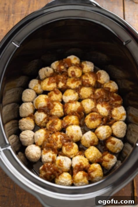 French Onion Soup poured over meatballs in an oval slow cooker.