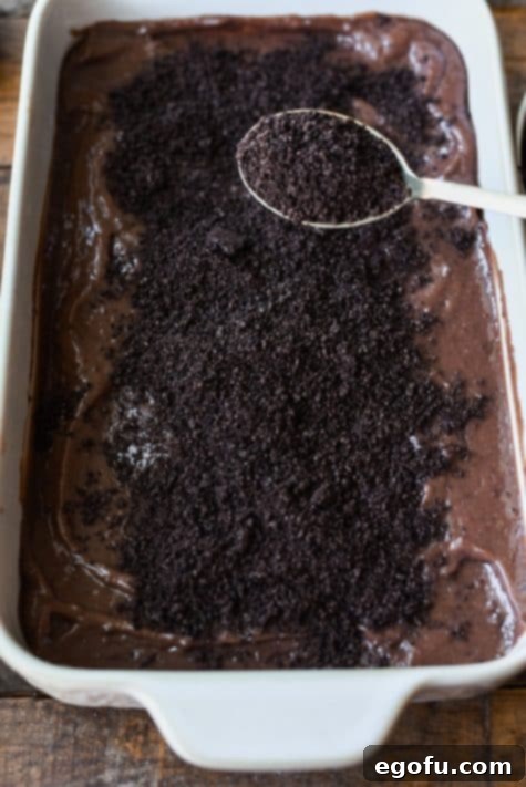 Oreo crumbs being spread over chocolate pudding.