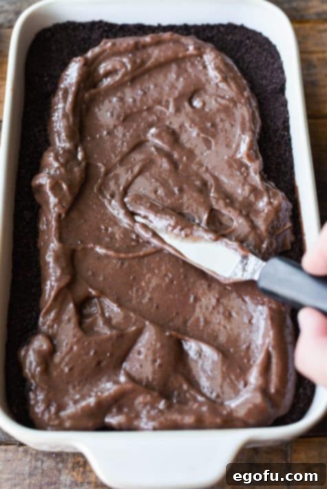 Chocolate pudding being spread over layers of more pudding and Oreo crumbs.
