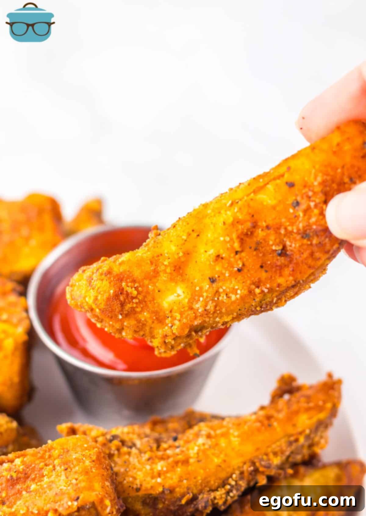 A hand holding a Potato Wedge about to dip it in ketchup.