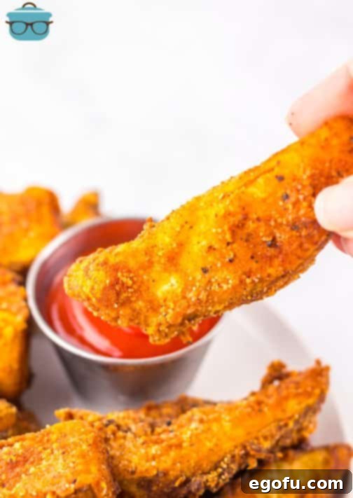 A hand holding a Potato Wedge about to dip it in ketchup.