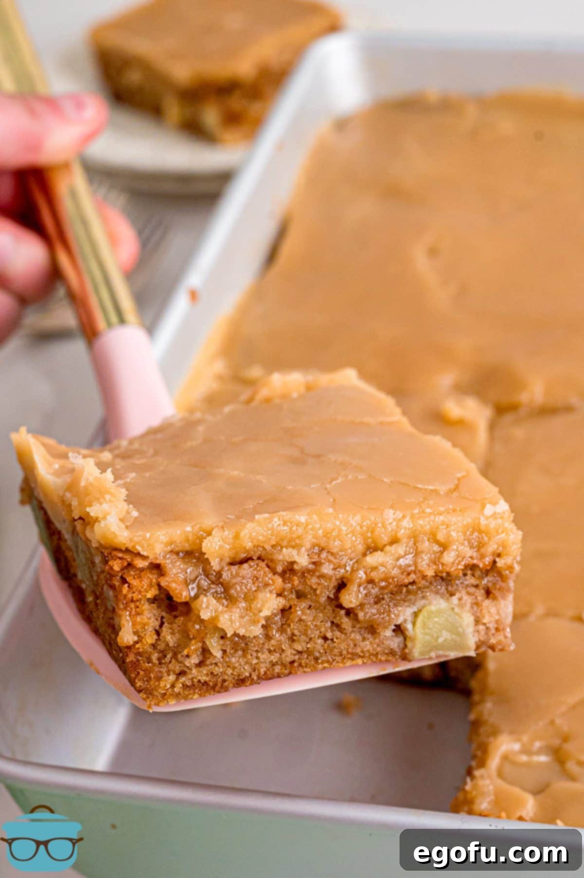 A serving utensil holding a slice of Apple Dapple Cake, showcasing its moist texture and rich brown sugar icing.