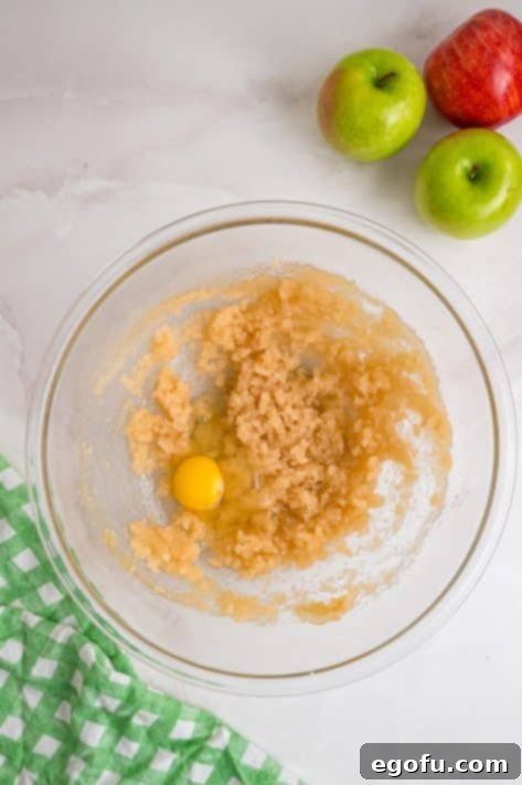A mixture of vegetable oil, granulated sugar, light brown sugar, and vanilla extract with eggs being added.