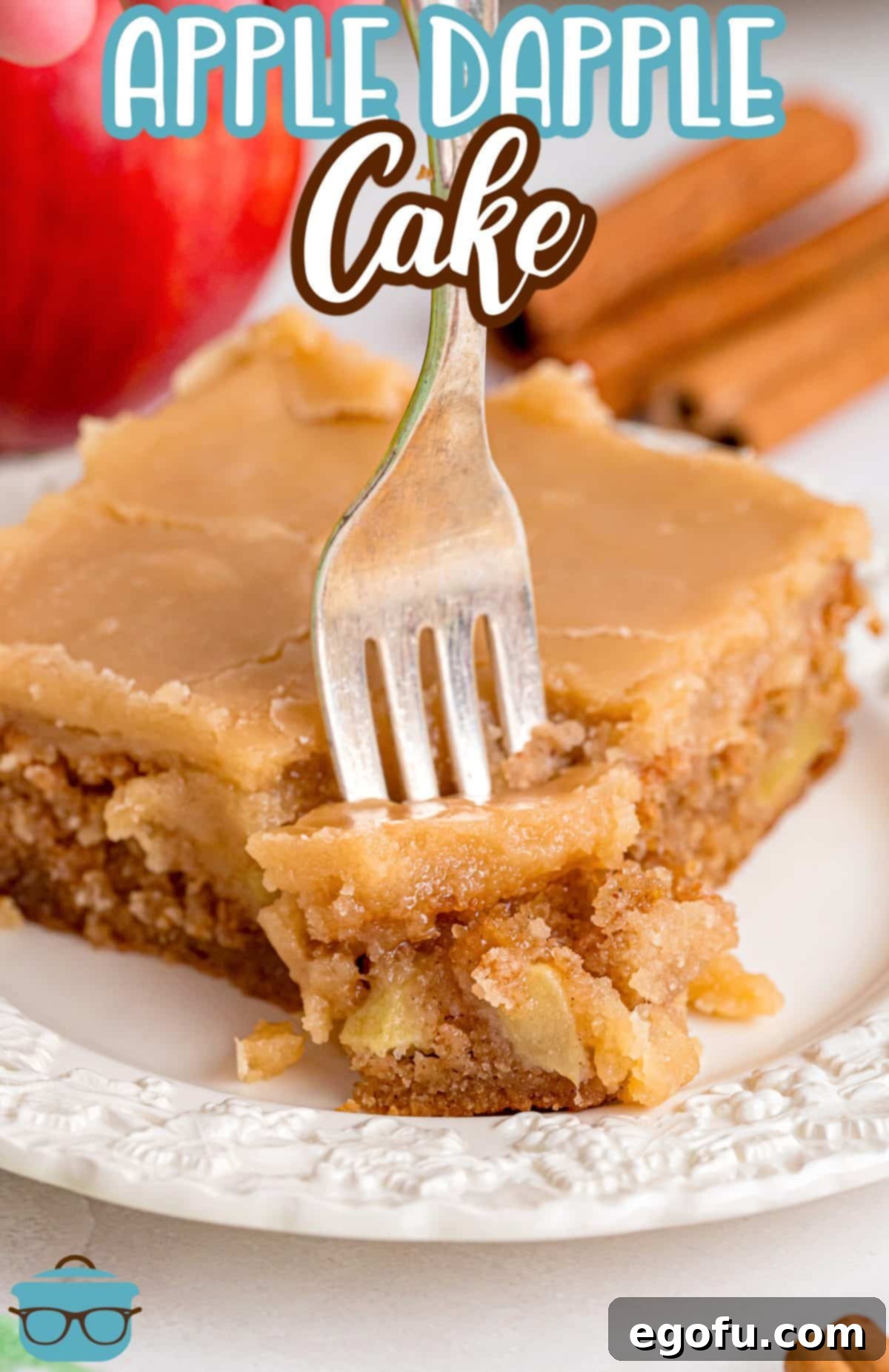 A fork taking a bite from a perfectly iced slice of Apple Dapple Cake, highlighting its soft texture.