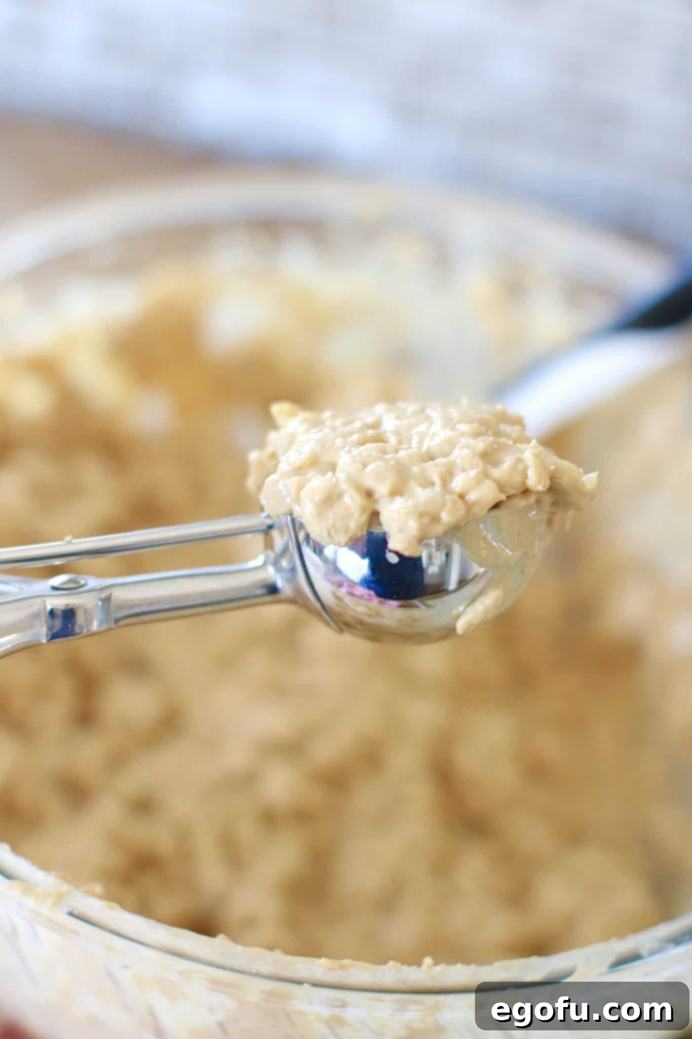 A spring-loaded cookie scooper scooping up some of the cookie batter, demonstrating the ease of portioning for uniform cookies.