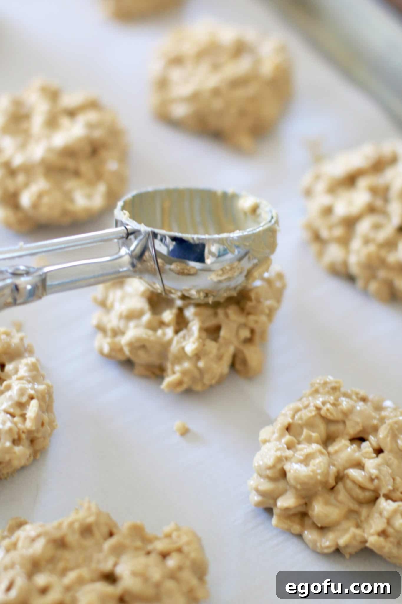 No bake peanut butter cookies on a cookie sheet being gently pressed by the back of a cookie scooper, showing the final shaping process.