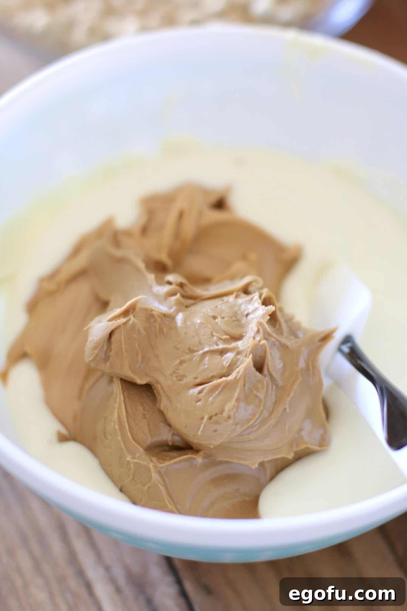 A bowl containing melted peanut butter, cookie butter, and white chocolate, forming a smooth, glossy mixture ready to be combined with the cereal.