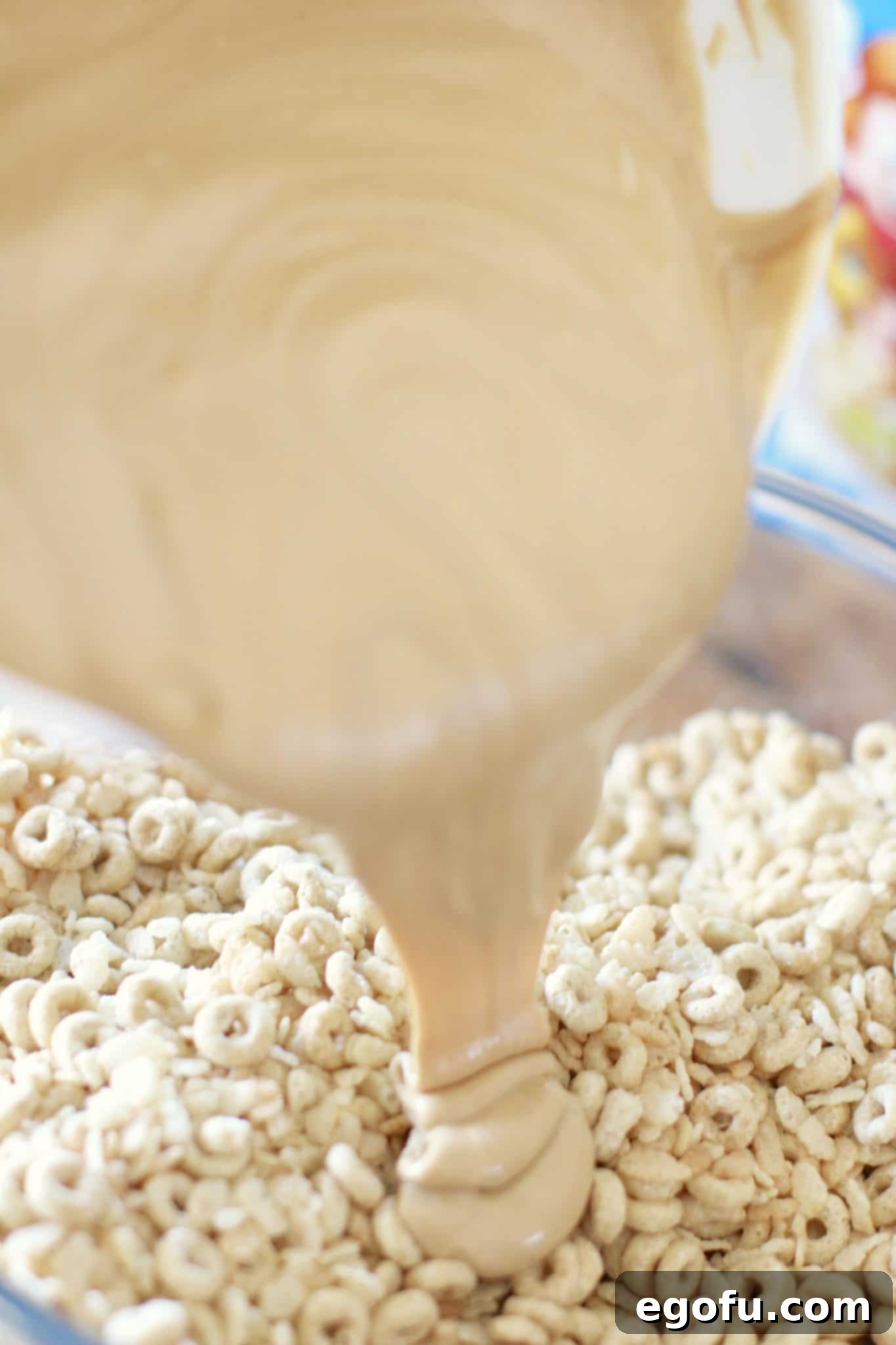 The peanut butter and white chocolate mixture being poured over the cheerios and Rice Krispies, ready to be stirred and combined.