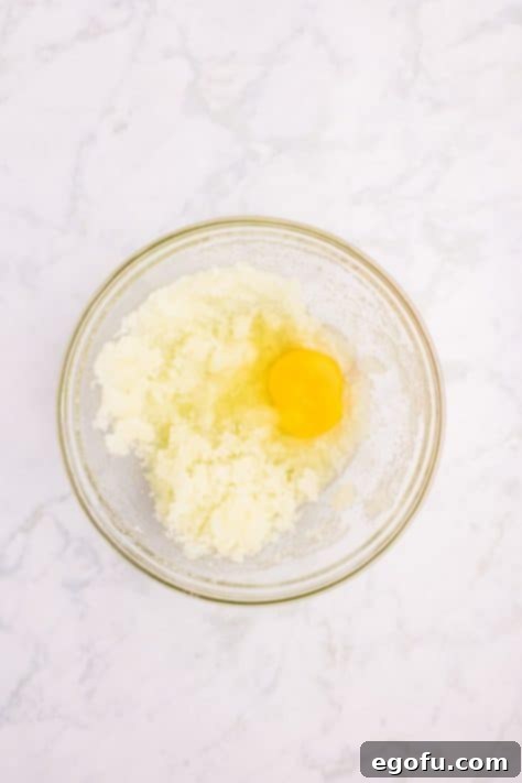Eggs being carefully beaten into the oil and sugar mixture in a large mixing bowl.