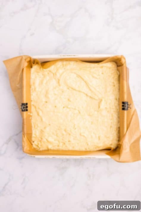 The initial layer of fluffy cake batter in a parchment-lined pan, topped generously with the flavorful cinnamon apple mixture.