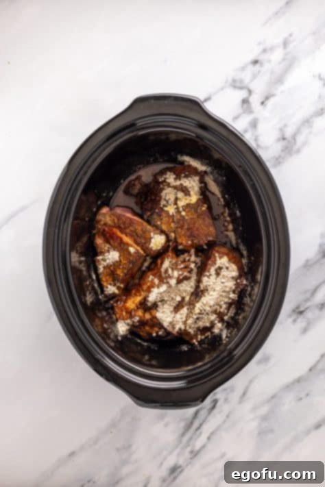 Seared beef and seasonings in a Crock Pot insert.