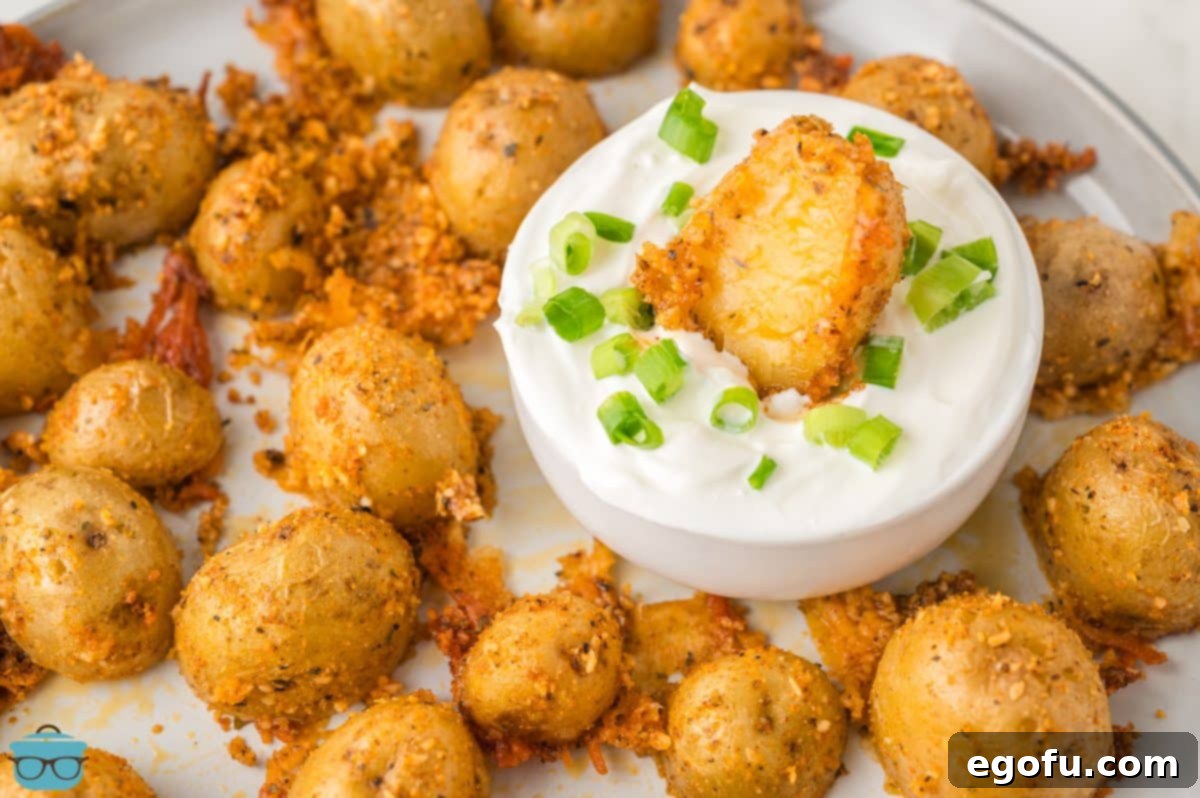 A plate of Crispy Parmesan Potatoes and dipping sauce with one in the sauce.