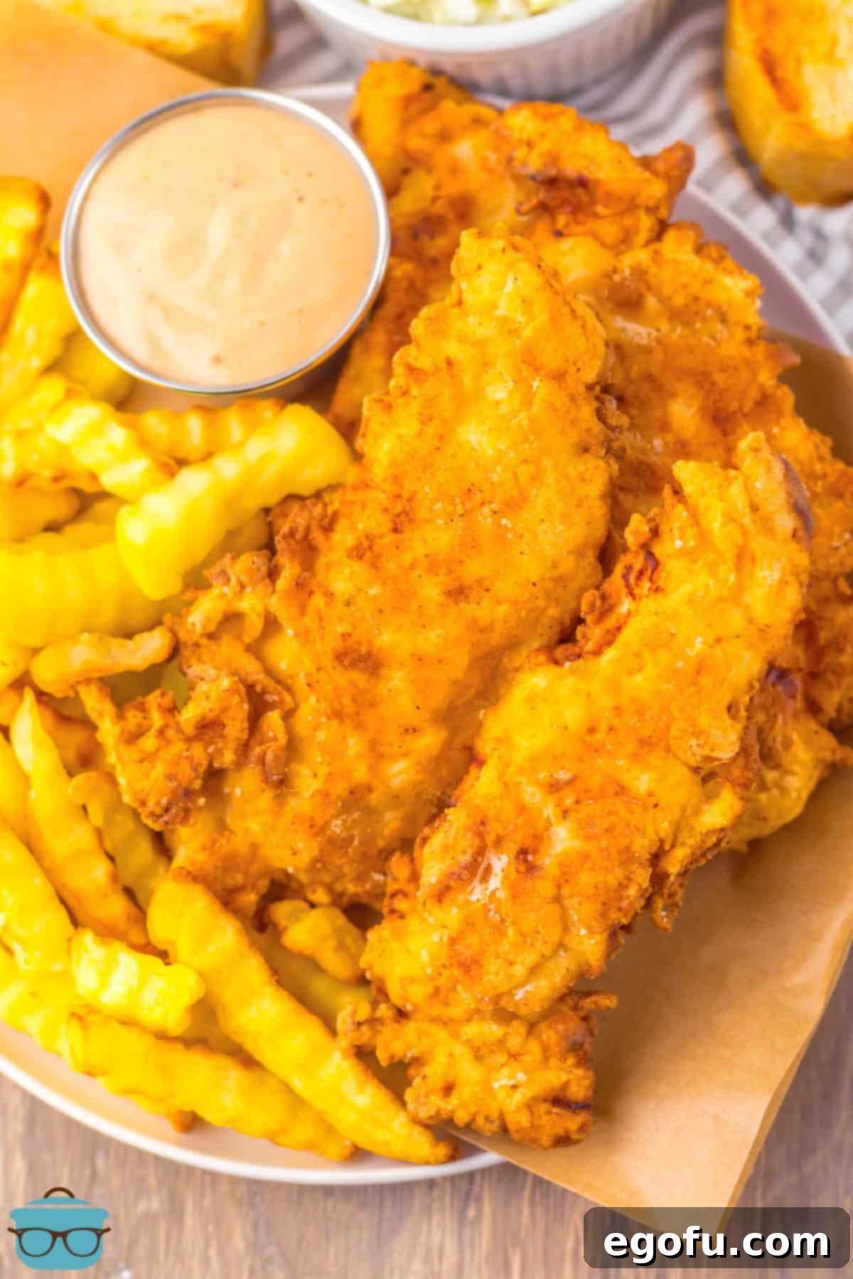 A beautifully arranged serving plate of golden-brown, crispy homemade Raising Cane's Chicken Fingers, accompanied by crinkle fries and a small bowl of the signature dipping sauce.