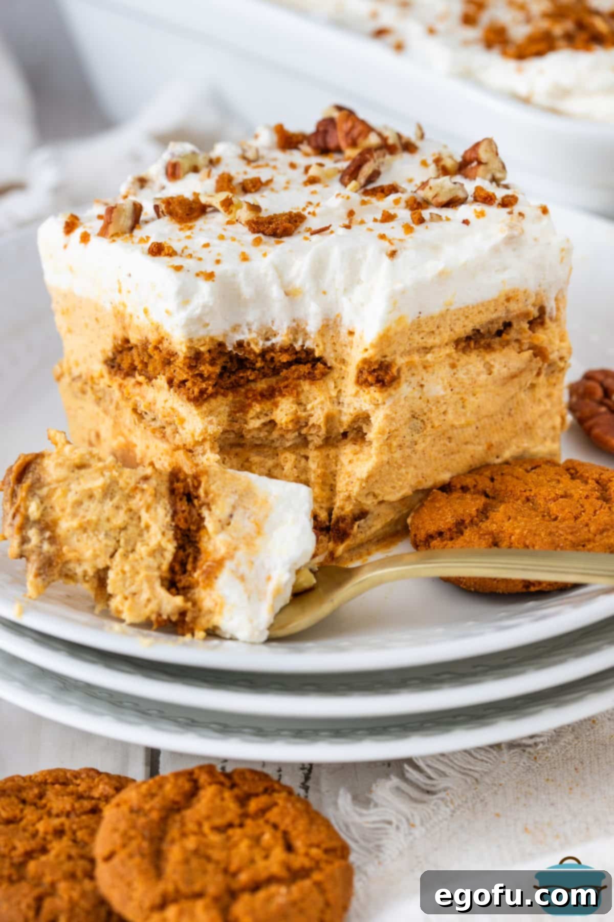 A fork holding a bite of No Bake Pumpkin Dessert on a few plates, showcasing the creamy pumpkin mousse and cookie layers.