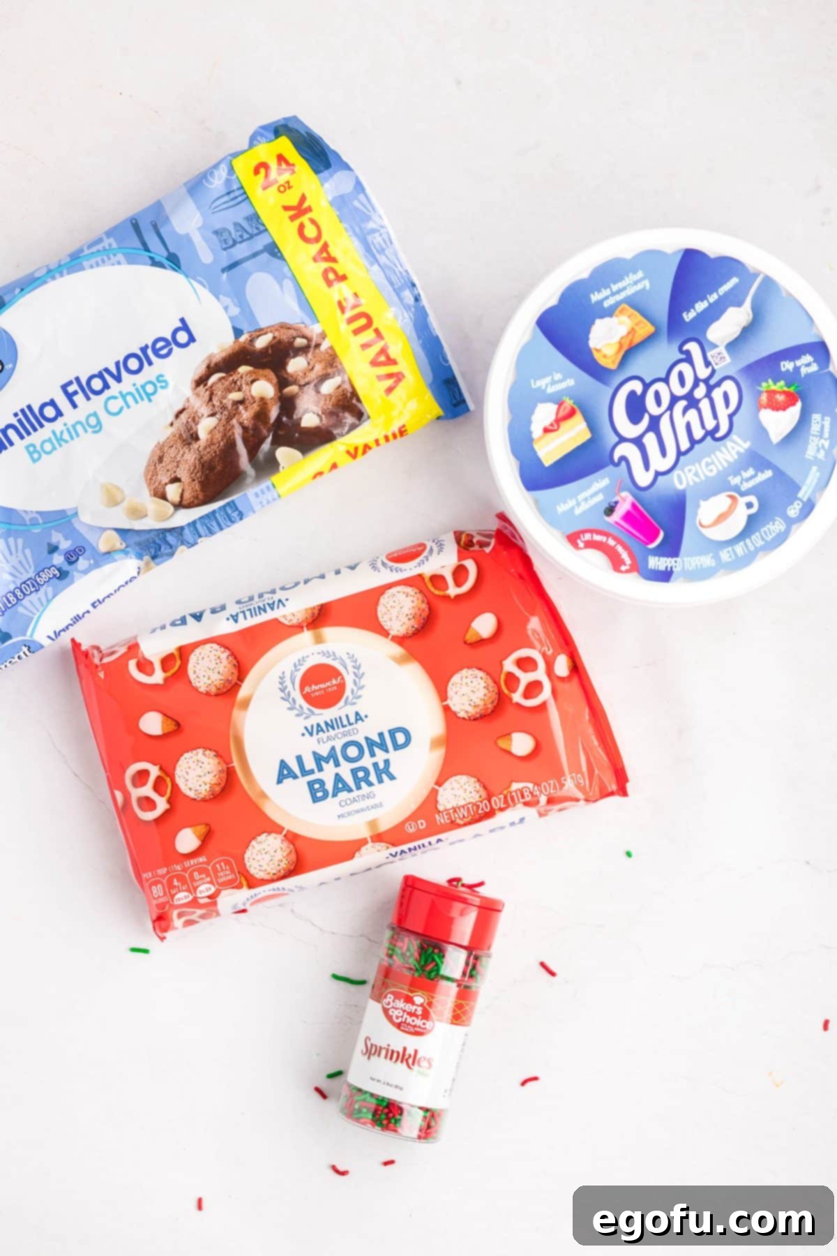 Creamy Cloud Bites 4 A collection of ingredients for Cool Whip Candy: vanilla almond bark, a tub of Cool Whip, white chocolate chips, and festive sprinkles laid out on a clean surface.