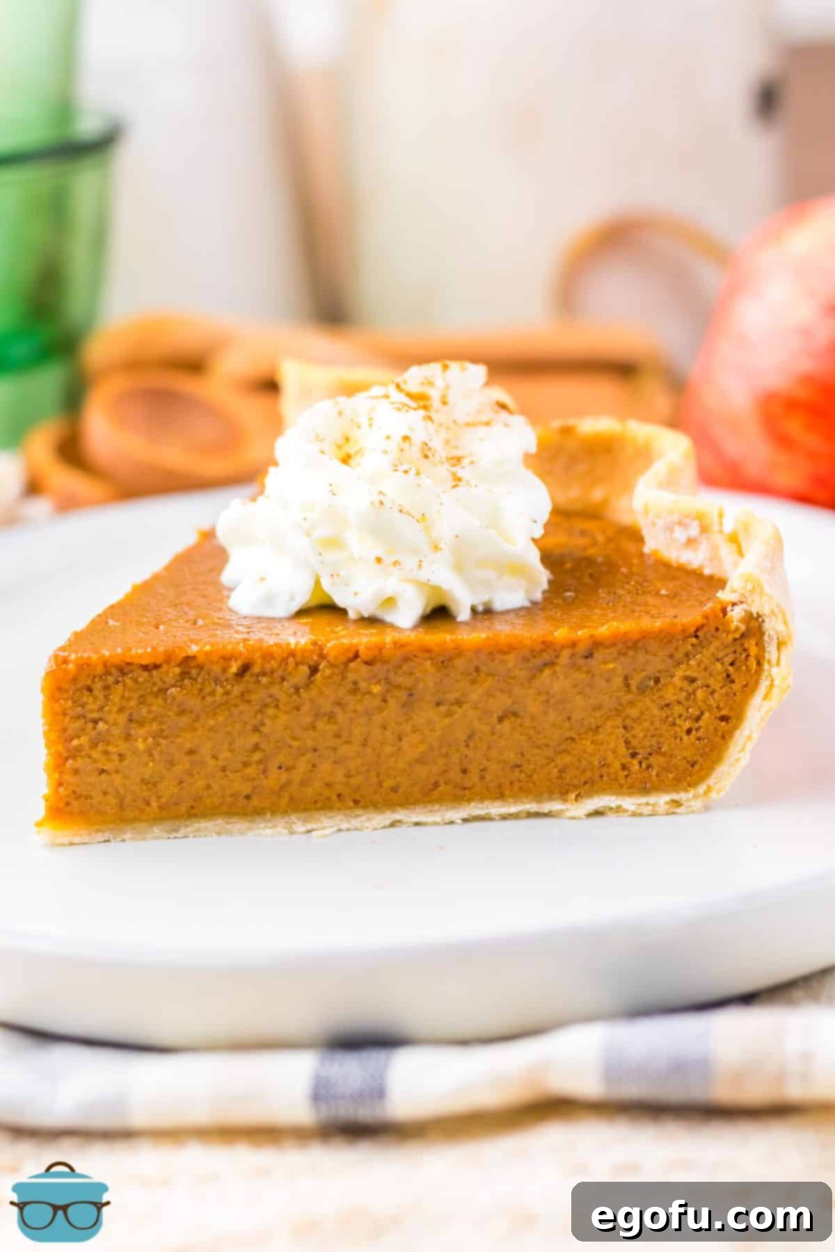 A white plate with a generous slice of Apple Butter Pie, topped with a dollop of fresh whipped cream and a sprinkle of cinnamon.