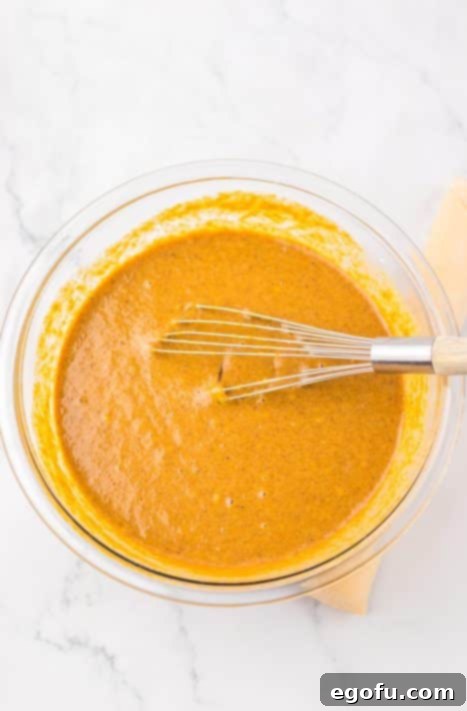 A whisk blending apple butter, eggs, sweetened condensed milk, vanilla, and flour in a mixing bowl until smooth.
