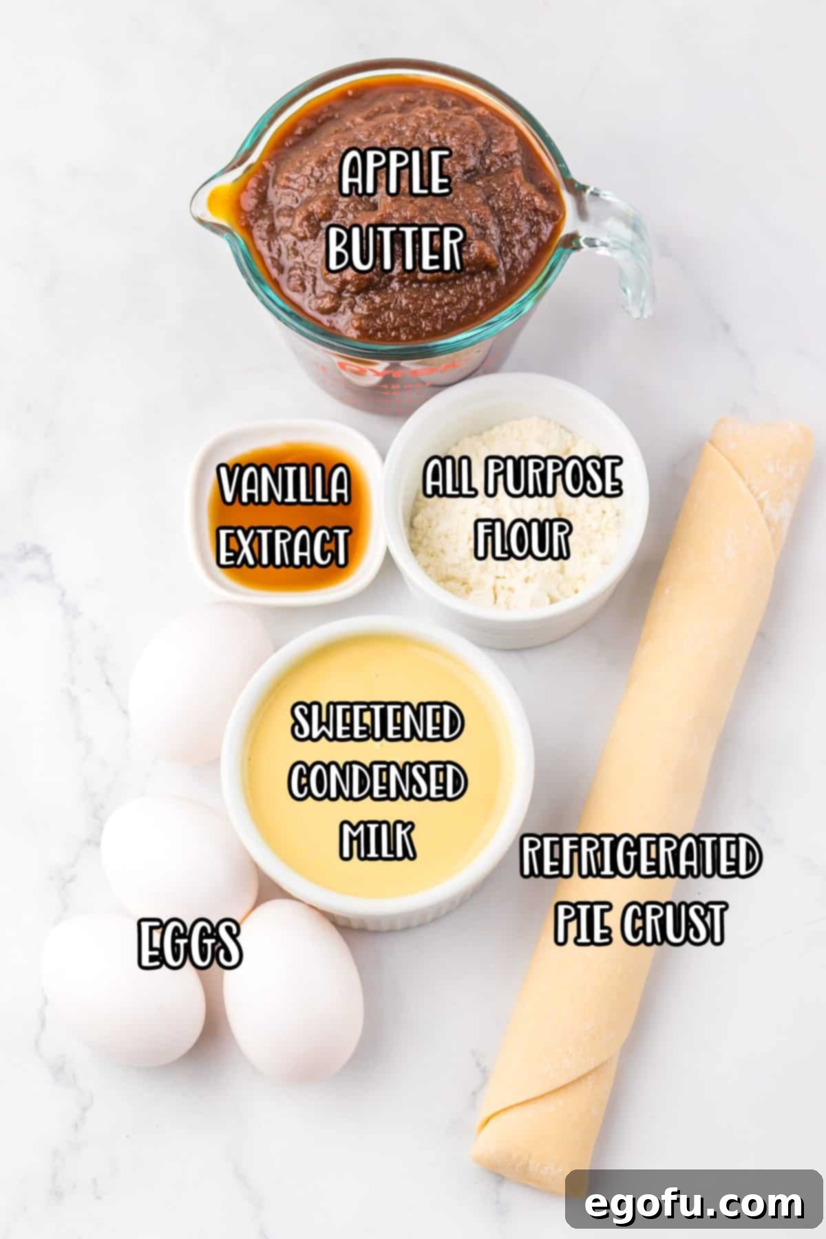 All the essential ingredients for Apple Butter Pie laid out: a jar of apple butter, a bag of all-purpose flour, a can of sweetened condensed milk, a bottle of vanilla extract, a carton of eggs, and a box of refrigerated pie crust.