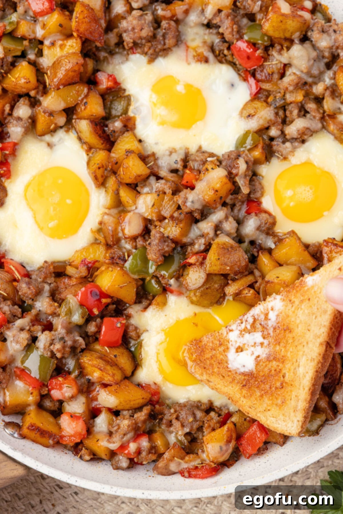 A piece of toast being dipped in Breakfast Hash in a skillet.