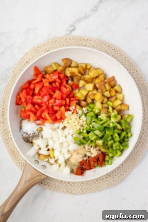 diced peppers, onion and seasonings added to a skillet with potatoes.
