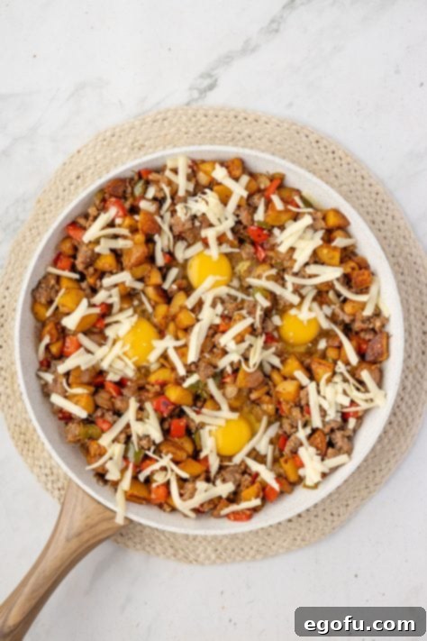 shredded cheddar cheese sprinkled on eggs and potatoes in a skillet.