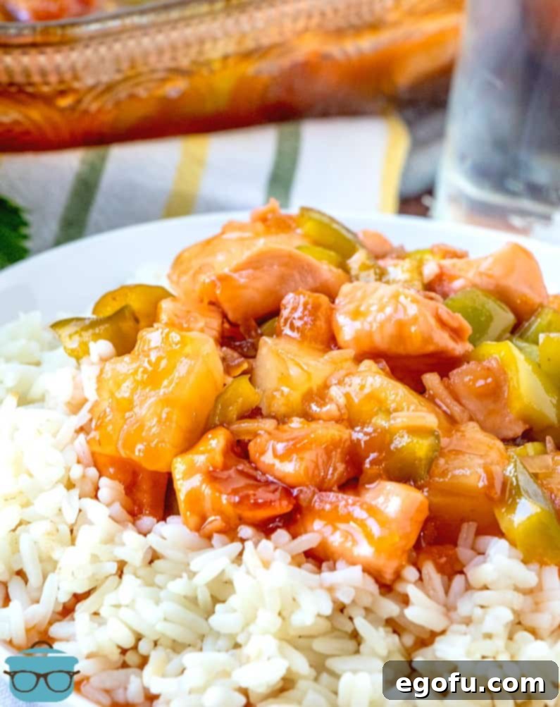 Sticky Sweet-Sour Chicken Bake 2 A serving of baked sweet and sour chicken with pineapple and green bell peppers, served over fluffy white rice on a clean white plate, with a baking dish blurred in the background, showcasing the vibrant colors and tender chicken.