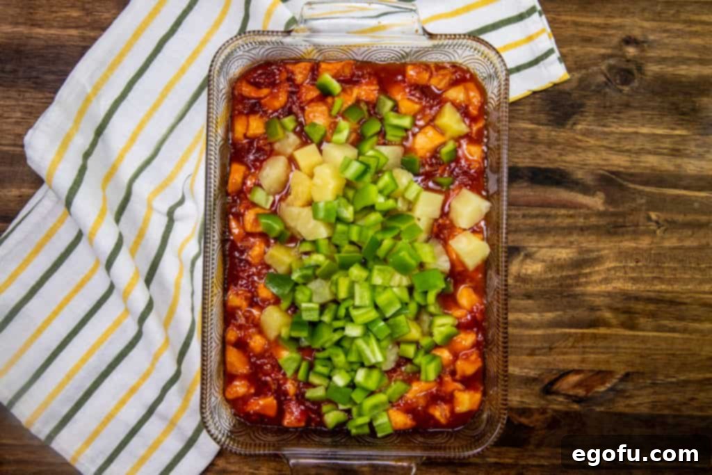 Sticky Sweet-Sour Chicken Bake 6 Diced green pepper and pineapple chunks being stirred into the apricot chicken mixture in a baking dish, adding vibrant color and fresh flavor.