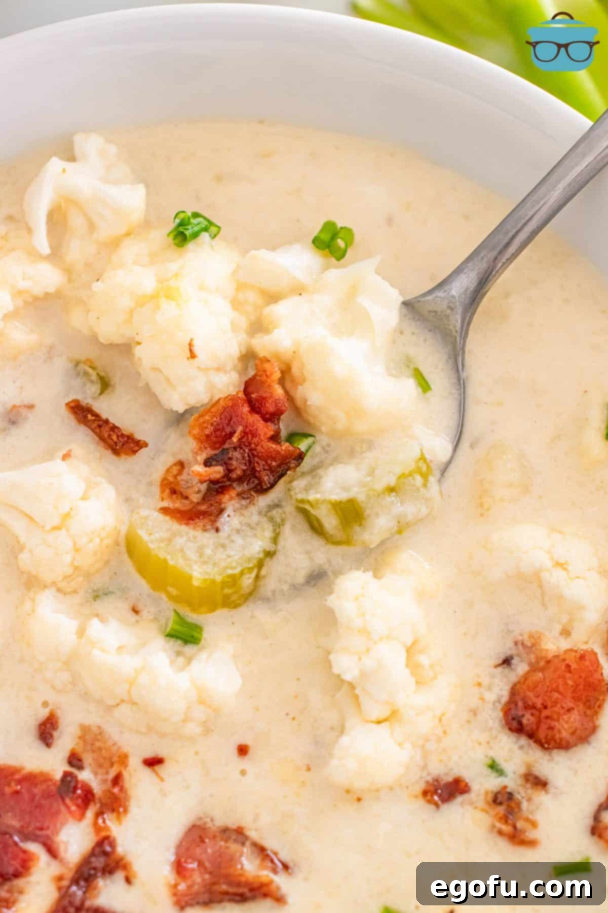 A spoon getting a bite of creamy, cheesy Loaded Cauliflower Soup, garnished with fresh chives and bacon.