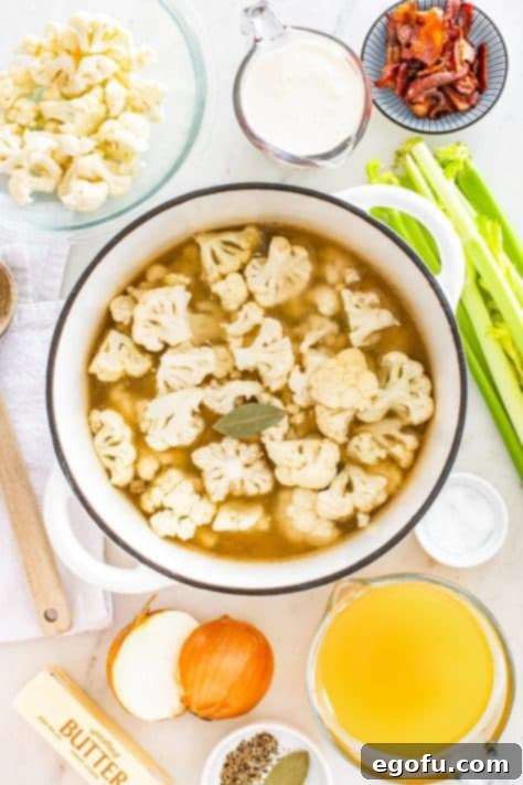 Cauliflower and broth added to a pot simmering with sautéed vegetables, preparing for the soup base.