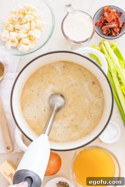 An immersion blender being used to puree a pot of cauliflower soup to desired consistency.