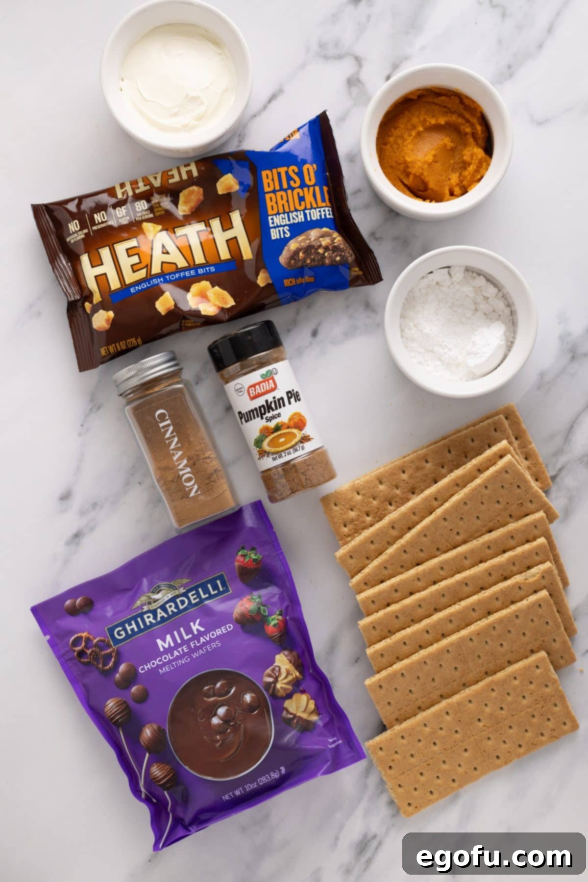 Cream cheese, powdered sugar, pumpkin puree, graham cracker crumbs, pumpkin pie spice, cinnamon, and milk chocolate melting wafers arranged as ingredients for Pumpkin Truffles.