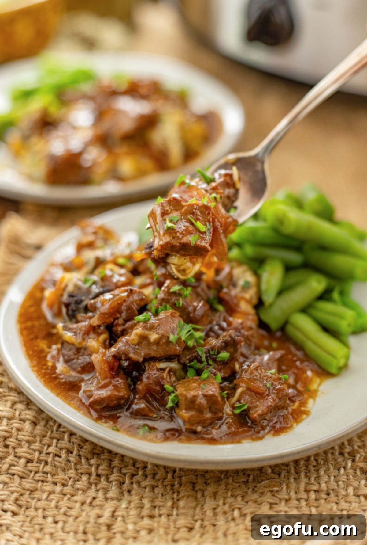 A fork getting a bite of French Onion Beef Tips from a plate.