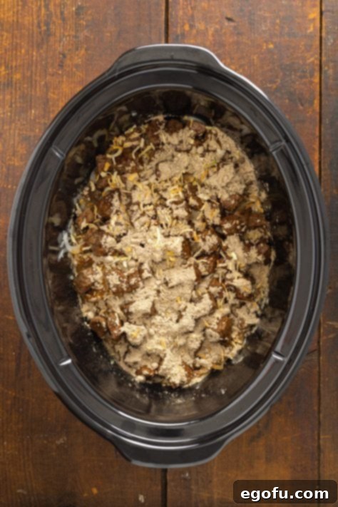 A Crockpot with onions, beef, and spice mixture.