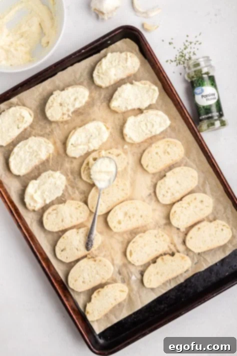 A mayo mixture being spread over bread slices on a lined baking sheet.