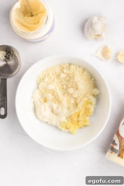 A bowl with mayonnaise, parmesan cheese, and minced garlic.